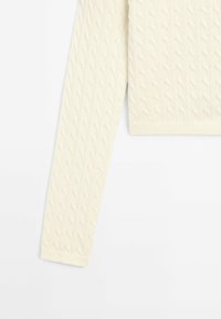 Cremefarbener Kabelstrickpullover mit strukturiertem Muster, gerippten Bündchen und verkürzter Länge. Weicher Stoff mit körpernaher Passform.