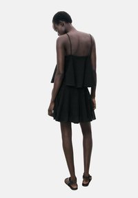 Schwarzes Kleid mit einem geschichteten, strukturierten Oberteil und einem ausgestellten Rock. Hergestellt aus strukturiertem Stoff, mit dünnen Trägern und minimalem Zubehör.