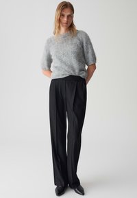 Pull gris flou à manches courtes associé à un pantalon large noir taille haute et des chaussures pointues noires. Design simple et moderne.