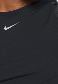 Černé sportovní tričko vyrobené z lehkého, hladkého materiálu, s kulatým výstřihem a reflexním logem Nike v levé horní části.