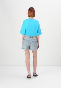 Krátký rukáv, jasně modré tričko spárované se světle modrými džíny s frayed lemy a béžovou koženou nášivkou na pase.