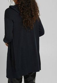 Navy oversized cardigan with a hood, long sleeves, and side slits. Made from textured fabric, featuring a relaxed fit and no visible fasteners.