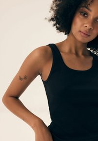 Czarny żebrowany top bez rękawów z okrągłym dekoltem. Posiada dopasowany krój, prezentujący tatuaż dwóch motyli na lewym ramieniu.