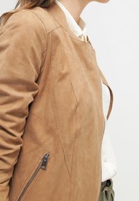 Zandkleurige suède jas met een aansluitend ontwerp, een zijrits, een gladde textuur en subtiele stikdetails.