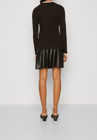 Svart långärmad topp med rund halsringning, kombinerad med en svart plisserad kjol i konstläder. Platta svarta klacksandaler fulländar outfiten.