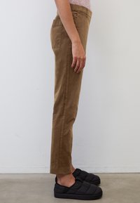 Bruine, rechte corduroy broeken met een soepele textuur en zijzakken, gecombineerd met zwarte instap, gewatteerde schoenen.