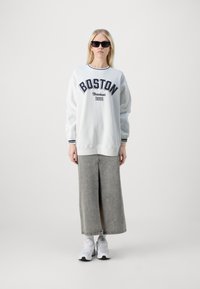 Sudadera gris con el estampado "BOSTON", combinada con una falda de mezclilla gris con una abertura delantera y zapatillas blancas. Gafas de sol negras como acento.