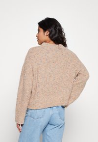 Maglione beige lavorato a maglia con una vestibilità comoda, caratterizzato da un motivo testurizzato di macchie multicolori. Rifinito con un collo rotondo e maniche lunghe.