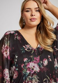 Blusa nera a fiori con scollatura a V, caratterizzata da motivi di fiori rosa e verdi, in tessuto leggero e trasparente, con maniche fluide e una finitura testurizzata.
