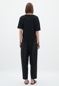 T-shirt noir à manches courtes et pantalon noir ample, présentant une silhouette décontractée et une texture en coton lisse, vu de dos.