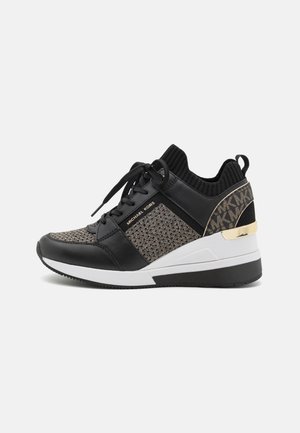 Sort og beige Michael Kors sneaker med strikket overdel, snørelukning foran, hvid sål, guld accenter og mærket hælpanel.