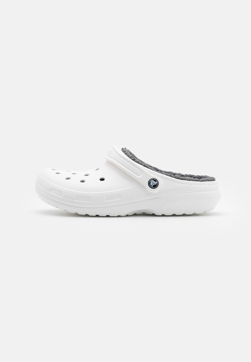 Sabot blanc à enfiler avec trous d’aération, doublure grise duveteuse et sangle de talon réglable avec logo circulaire sur le côté.