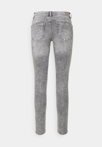 Jeans ajustados de mezclilla gris con un acabado desgastado, cinco bolsillos y una etiqueta en la cintura. El diseño presenta un corte ceñido y un largo hasta los tobillos.