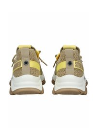 Sneakers beige e bianchi con retro testurizzato, dettagli gialli e suole in gomma robuste. Presentano una cinghia con testo del logo e lacci elastici.