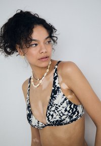 Bikini top s čiernobielym vzorom a hlbokým V-výstrihom, vyrobený z hladkej látky. Obsahuje tenké nastaviteľné ramienka a široký pás.