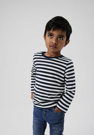 T-shirt a maniche lunghe a righe blu e bianche, scollo rotondo, abbinato a jeans blu. Il tessuto sembra morbido e informale con una vestibilità rilassata.