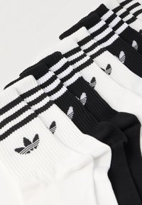 Baltos ir juodos spalvos kojinės su gofruota faktūra, viršuje trys horizontalios juostos ir juodas logotipas ant kiekvienos kojinės.