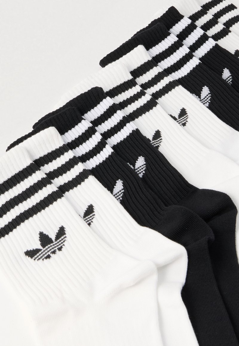 Calze bianche e nere con texture a coste, caratterizzate da tre strisce orizzontali nella parte superiore e un logo nero su ogni calza.