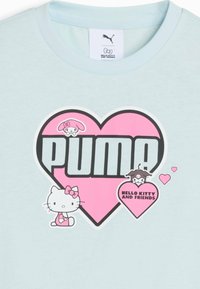 Camisa azul claro con un gran corazón rosa que presenta el texto "PUMA", personajes de Hello Kitty y amigos, y un corazón más pequeño con el texto "Hello Kitty and Friends".