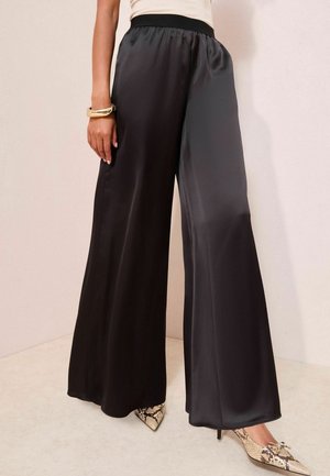 Black satin wide-leg pants with a stretchy waistband. Paired with pointed snake-print heels. Smooth texture, flowing silhouette.