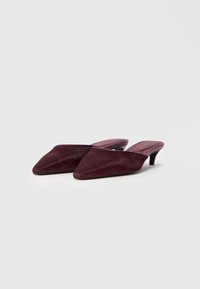 Mūles ar izteiktu purngalu, izgatavotas no tumši bordo krāsas kažokādas materiāla, ar elegantu dizainu un zemu melnu papēdi.