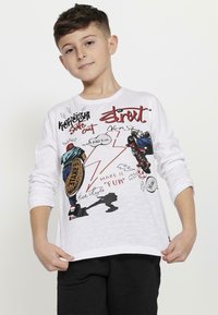 Witte lange мouw T-shirt met kleurrijke grafische prints van skateboardfiguren, dynamische tekst en abstracte vormen. Zacht, katoenen materiaal.