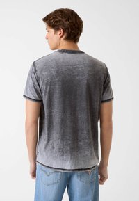 Szara aksamitna koszulka o gładkiej fakturze, krótkich rękawach, okrągłym dekolcie i subtelnym gradiencie od ciemnoszarego do jasnoszarego przy krawędzi.