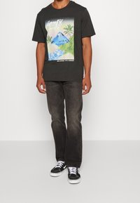 Svart grafisk t-shirt med färggrafisk bergstryck, korta ärmar och rund halsringning, matchad med mörka jeans och svarta sneakers.