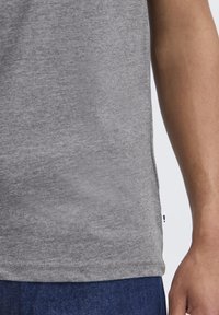 Gray cotton T-shirt with a rounded hem, visible side seam, and small label tag. Fabric has a smooth texture and simple design.