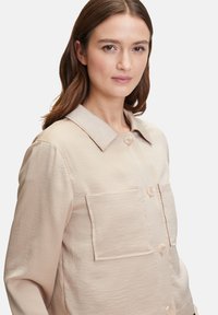 Lichtbeige button-up jas met een kraag, twee voorzakken en een gestructureerde stof. Kenmerkt zich door ronde knopen en een relaxed fit ontwerp.