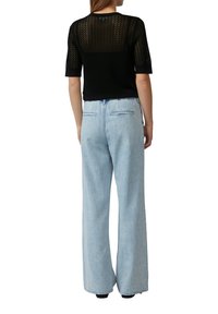 Zwarte gebreide top met korte mouwen en chevronpatroon; lichtblauwe high-waisted wijde jeans met twee achterzakken en een denimtextuur.