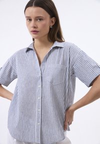 Camicia a maniche corte a righe blu e bianche, con chiusura a bottoni, colletto e taschino sul petto. Realizzata in un tessuto leggero.