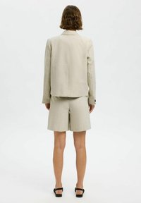 Lys beige blazer med et moderne snit, parret med matchende skræddersyede shorts. Har subtil tekstur og knapdetaljer på ærmerne.
