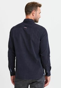Marineblauwe langemouwen shirt met een button-down kraag, donker gestructureerde stof en contrasterende binnenmanchetten. Kleine accent bij de achterkant van de halslijn.