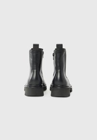Botas de tobillo de cuero negro con un acabado suave, paneles laterales elásticos y una suela gruesa. Costuras detalladas y tiradores en la parte trasera.