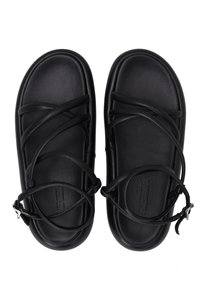 Schwarze Ledersandalen mit flacher Sohle, ausgestattet mit sich kreuzenden Riemen und einer Schnalle an einer Seite. Glatte Textur und minimalistisches Design.