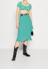 Grønt blomsterprintet todelt sæt med en cropped top med pufærmer og en midilengde nederdel, kombineret med sorte cowboystøvler.