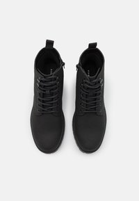 Botines negros hasta el tobillo con acabado mate suave, con diseño de cordones, suelas de goma resistentes y una pestaña de tirón en la parte posterior para facilitar el calzado.