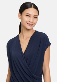 Navy blue wrap top in soft fabric with a deep V-neck and short sleeves, featuring draped detailing at the front.