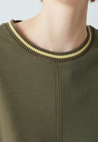 Olive green sweatshirt featuring a round neckline with dark and light striped ribbed accents. Smooth fabric with a subtle texture.