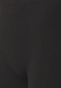 Zwarte geribde leggings met een gladde textuur, een hoog tailleontwerp en een aansluitende vorm die tot de enkel reikt.