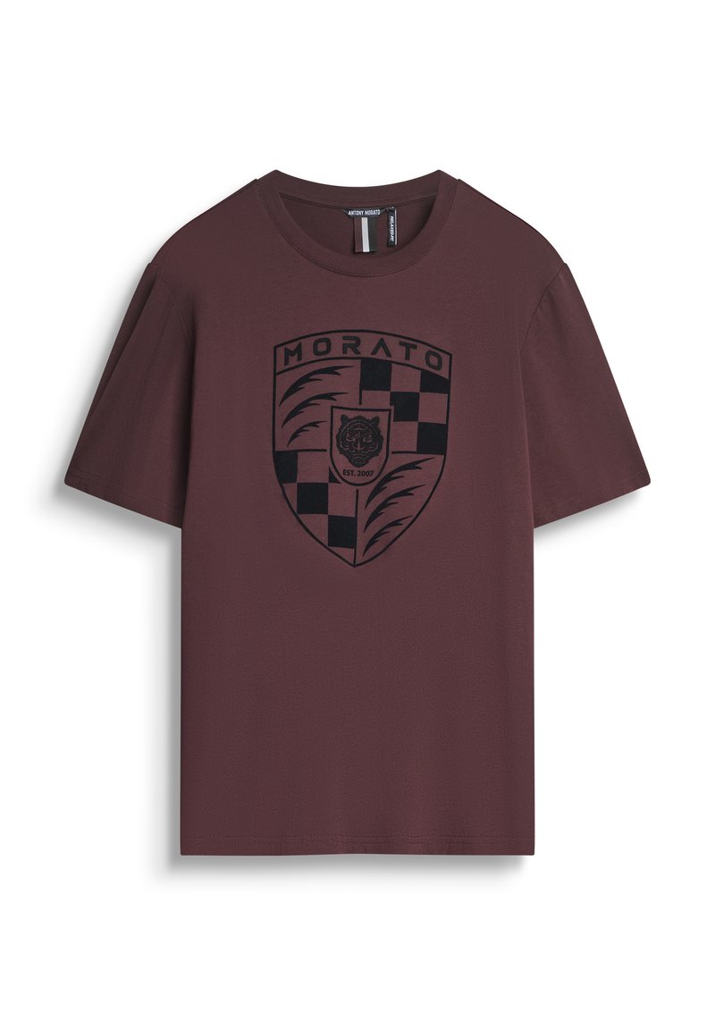 Camiseta marrón de algodón, con un logo de escudo negro que presenta un tigre y un patrón de cuadros. Mangas cortas, diseño de cuello redondo.