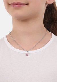 Collana in argento con pendente a forma di stella rosa, decorata con diversi piccoli gemellini, indossata sopra una maglietta bianca.
