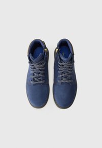 Par de botas de camurça azul com atacadores, colarinhos almofadados e atacadores com padrão, sobre um fundo branco simples.