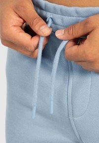 Himmelblaue Jogginghosen mit strukturiertem Stoff. Die Kordeln mit Kunststoffspitzen werden angepasst. Enthält Seitentaschen.