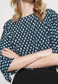 Haut bleu et noir à motif avec un design de vagues, featuring des manches amples et un col rond, associé à une jupe noire.