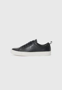 Fekete bőrsneaker lekerekített orral, fehér gumitalppal, fűzős elejével és dombornyomott logó részlettel az oldalon. Simább textúrájú.