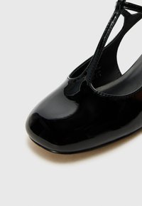 Black patent leather shoe with a rounded toe and cut-out design. Smooth texture, glossy finish, and low heel visible in the image.