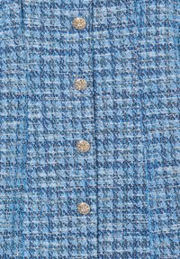Tessuto di colore blu chiaro con una trama a quadri, caratterizzato da quattro bottoni metallici. Il design tessuto aggiunge profondità e interesse.
