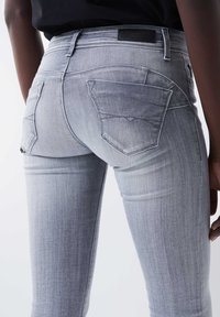 Hellgraue Jeans aus Denim mit tailliertem Design, zwei Gesäßtaschen und subtiler Verwaschung. Der Stoff ist glatt und hat eine leicht dehnbare Textur.